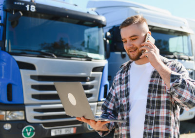 Man holding a laptop and talking on phone with semi trucks